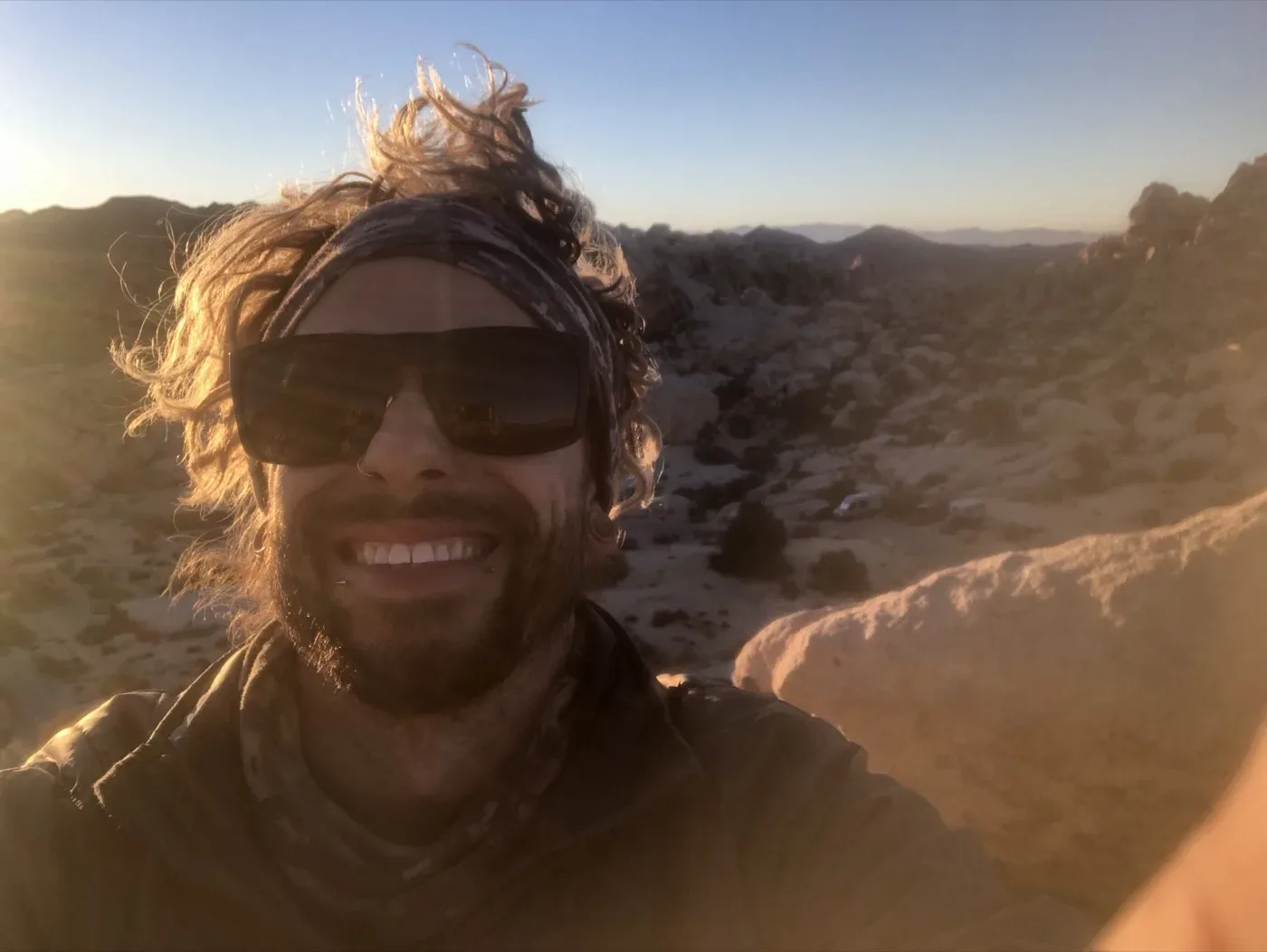 Randy smiling in sunglasses on a rock face at golden hour